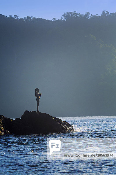 Gemischtrassige Frau steht auf einem Felsen über dem Meer