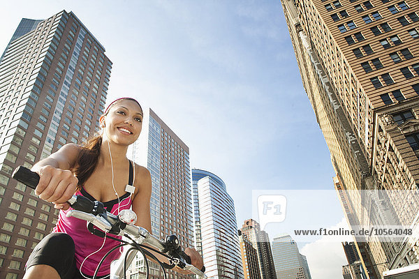 Hispanische Frau fährt Fahrrad unter Hochhäusern