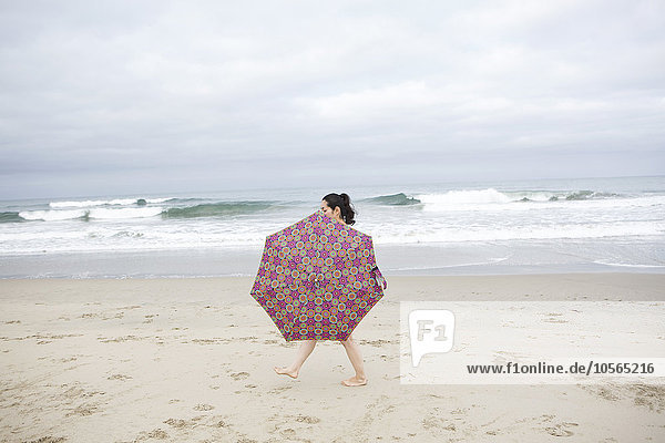 Frau geht mit Regenschirm am Strand spazieren