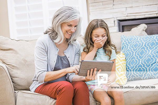 Kaukasische Großmutter und Enkelin benutzen ein digitales Tablet auf dem Sofa