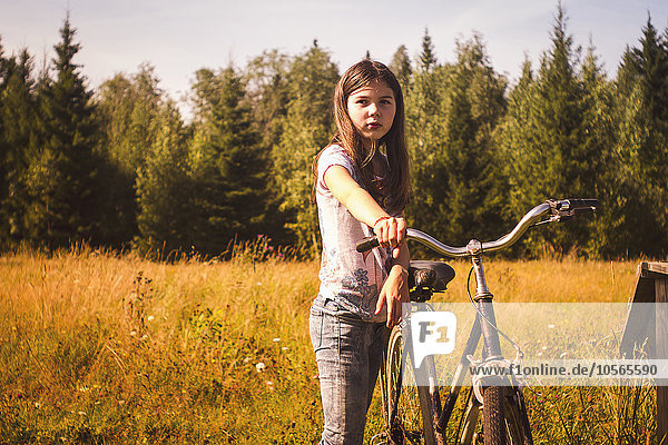 Kaukasisches Teenager-Mädchen  das ein Fahrrad auf einem Feld schiebt