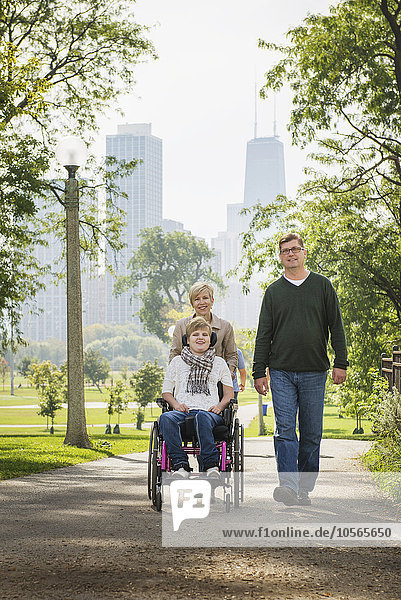 Eltern schieben querschnittsgelähmte Tochter im Rollstuhl