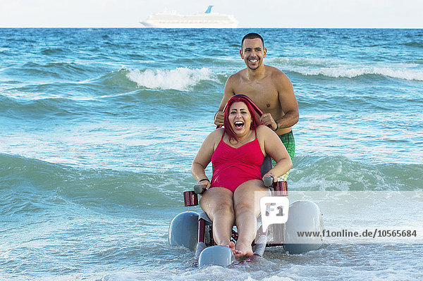 Mann schiebt querschnittsgelähmte Freundin im Rollstuhl über den Strand