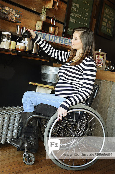 Querschnittsgelähmte Frau im Rollstuhl schenkt im Café Kaffee ein