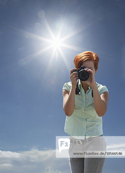 Caucasian woman photographing under blue sky
