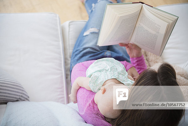 Mutter liest ein Buch und hält ihre kleine Tochter