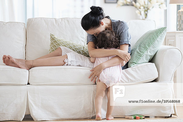 Mutter  die ihre kleine Tochter auf dem Sofa umarmt