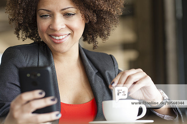 Gemischtrassige Frau benutzt Mobiltelefon in einem Café