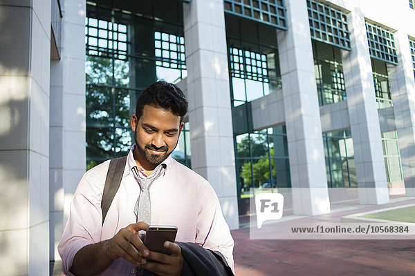 Indischer Geschäftsmann benutzt Mobiltelefon vor Bürogebäude