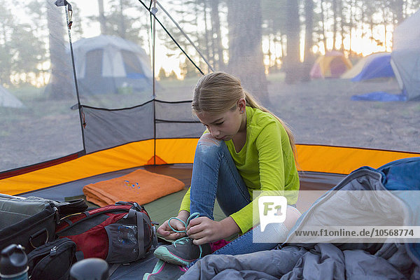 Caucasian girl tying shoes in camping tent