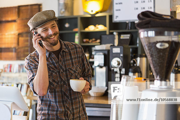 Kaukasischer Mann  der in einem Café mit seinem Handy telefoniert