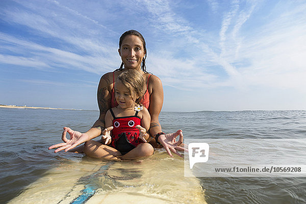 Mutter und Tochter meditieren auf dem Surfbrett