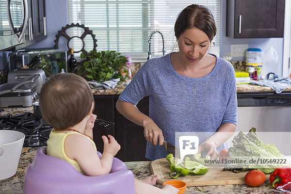 Gemischtrassige Mutter hackt mit ihrer Tochter in der Küche Gemüse