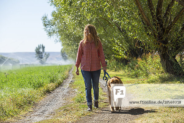 Kaukasische Frau geht mit Hund auf unbefestigtem Weg spazieren