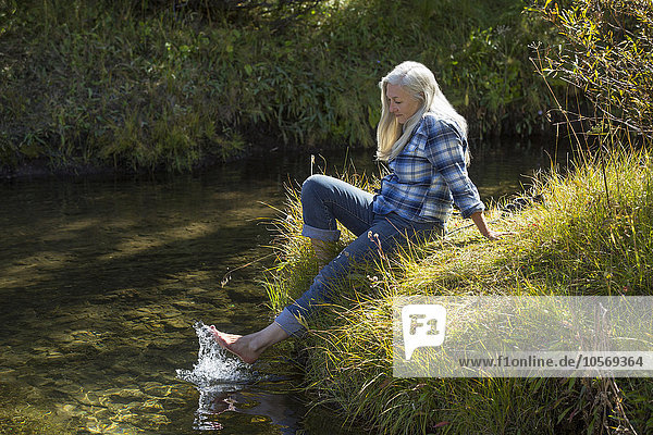 Kaukasische Frau plantscht mit den Füßen im Fluss