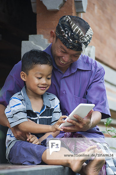 Asiatischer Vater und Sohn benutzen ein Mobiltelefon im Freien