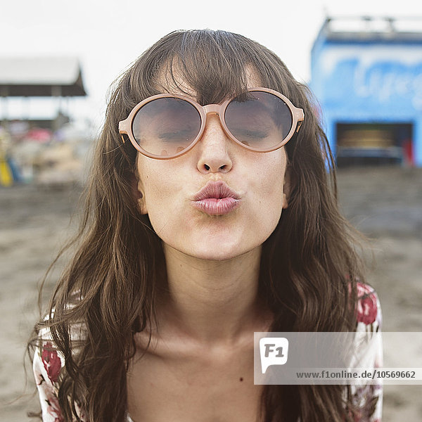 Kaukasische Frau mit Sonnenbrille  die sich am Strand zum Kuss verbeugt