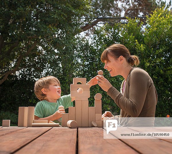 Mutter und Sohn spielen mit Holzbausteinen im Garten