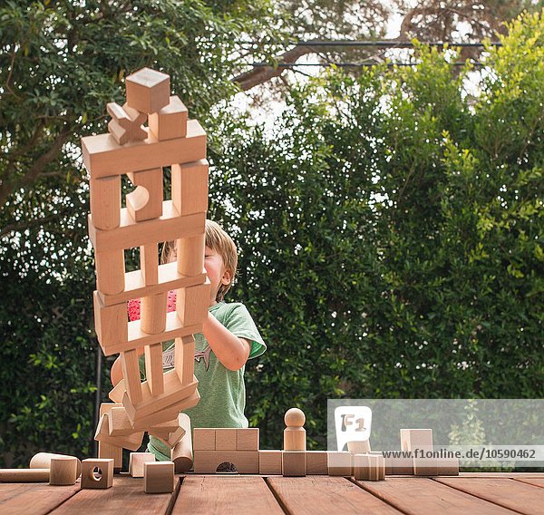 Junge schiebt über Holzkonstruktion aus Bauklötzen  im Freien