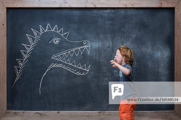 Kleiner Junge brüllt auf Dinosaurierzeichnung auf Tafel
