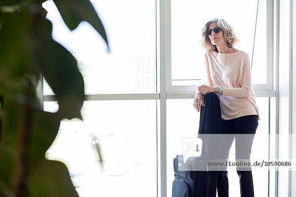 Senior Geschäftsfrau wartet mit Rollkoffer im Bürogebäude