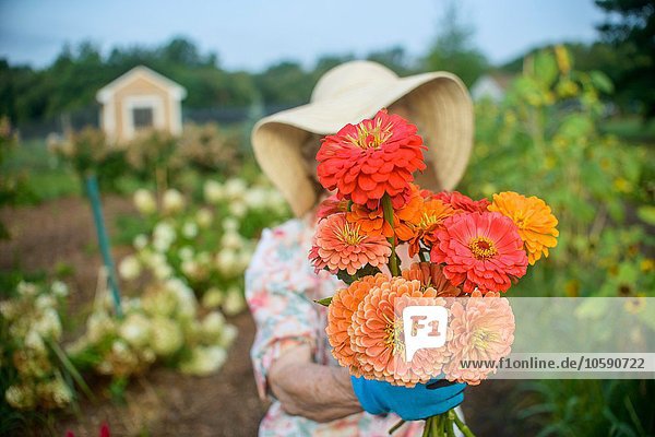 Seniorin mit Blumen vor dem Gesicht auf dem Bauernhof