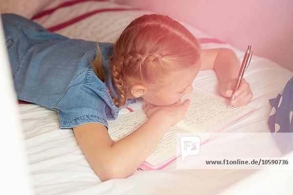 High angle view of girl lying on bed writing in notebook