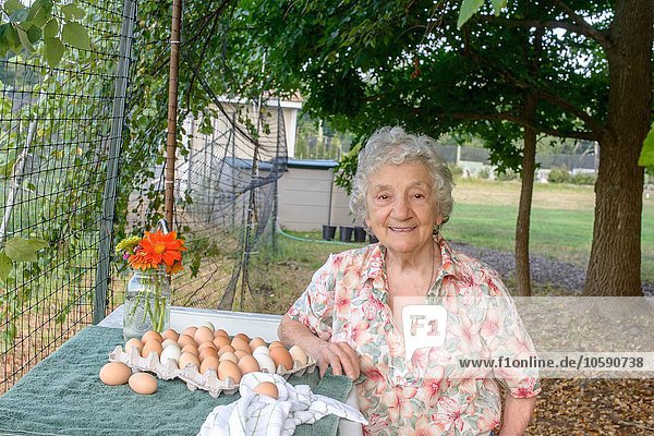 Senior woman posing beside tray of eggs on farm