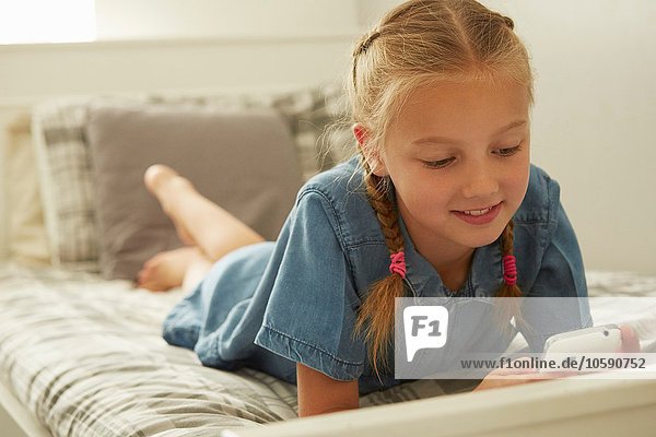 Girl lying on bed looking down at smartphone smilinhg