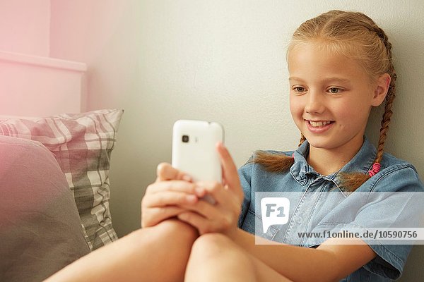 Mädchen sitzt an der Wand und schaut lächelnd auf das Smartphone.