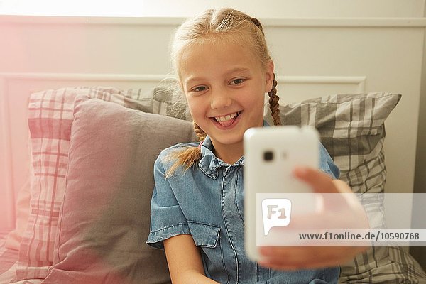Mädchen sitzt auf dem Bett mit dem Smartphone zu nehmen Selfie lächeln