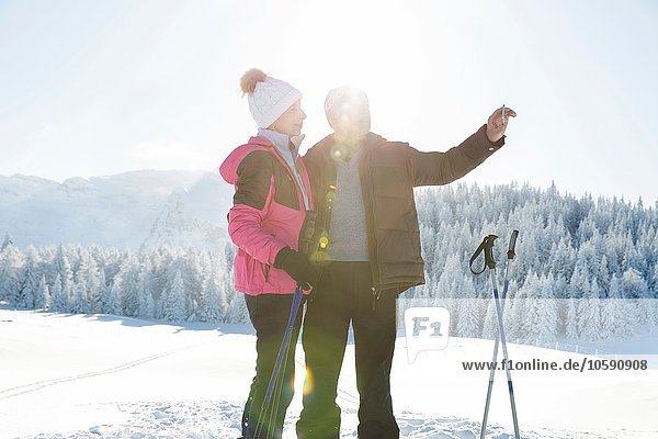 Senior couple on snowy landscape using smartphone to take photograph  Sattelbergalm  Tyrol  Austria