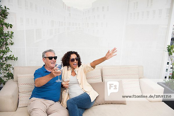 Senior Mann und Frau winken vom Sofa auf der Terrasse