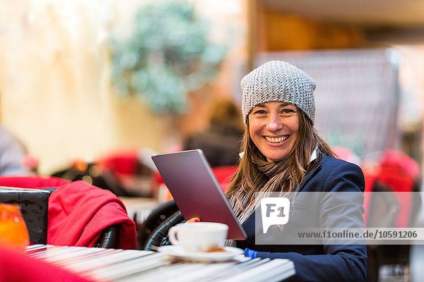 Porträt einer reifen Frau mit digitalem Tablett im Straßencafé