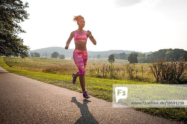 Young female runner running along rural park path