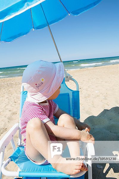 Weibliches Kleinkind schaut vom Strandkorb aus über die Schulter.