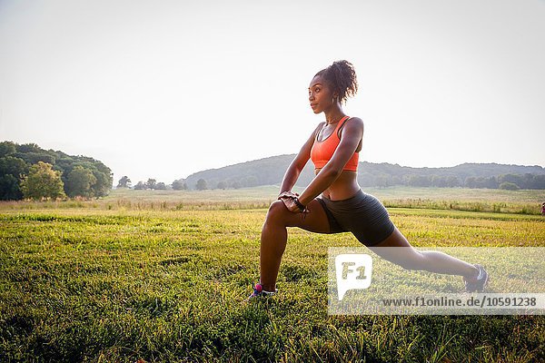 Young female runner stretching in rural park