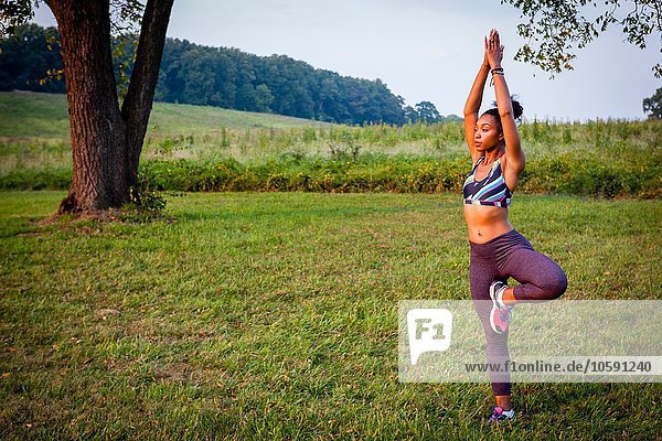 Young woman practicing yoga tree pose in rural park
