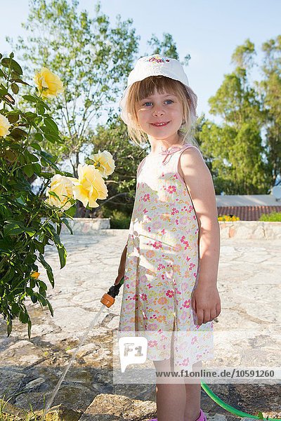 Porträt eines Mädchens mit Sonnenhut und gießenden Rosen