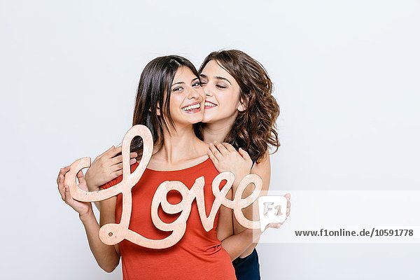 Lesbian couple holding the word love  looking at camera smiling