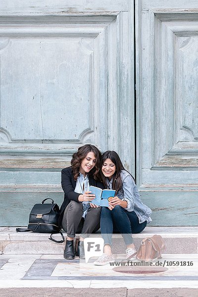 Lesbian couple sitting in oversized church doorway looking at book  Piazza Santa Maria Novella  Florence  Tuscany  Italy