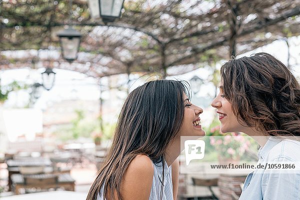Lesbisches Paar in pflanzenbedecktem Bogen von Angesicht zu Angesicht lächelnd  Florenz  Toskana  Italien