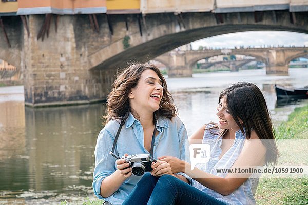 Lesbian couple sitting together looking at digital camera laughing  in front of Ponte Vecchio  Florence  Tuscany  Italy