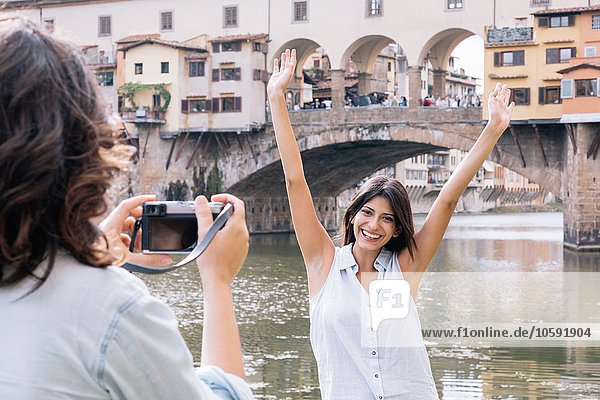 Young woman arms raised posing for photograph in front of Ponte Vecchio and river Arno  Florence  Tuscany  Italy
