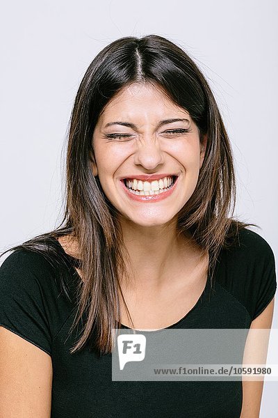 Head and shoulder portrait of young woman eyes closed toothy smile