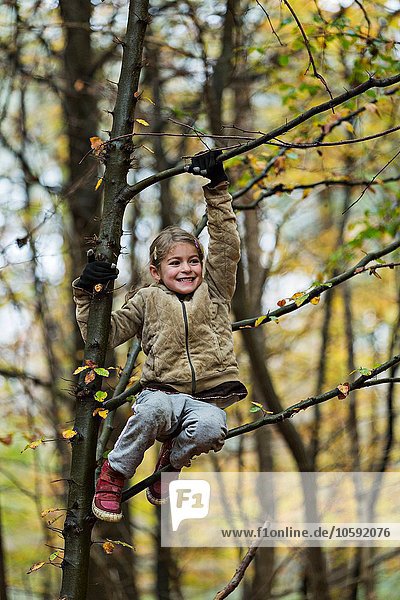 Girl hanging on to tree branch in autumn forest