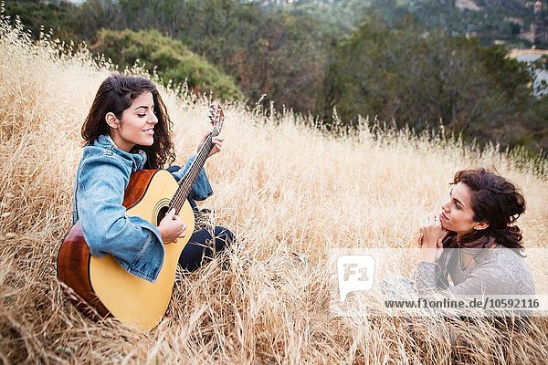 Young woman in long grass playing guitar to friend  Woodland Hills  California  USA