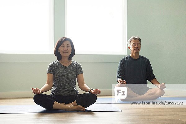 Erwachsenes Paar sitzend im Kreuzbein auf Yogamatte meditierende Augen geschlossen