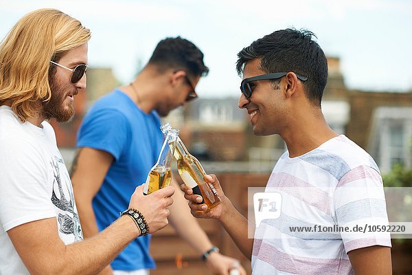 Zwei männliche Freunde stoßen mit Flaschenbier auf der Dachparty an.