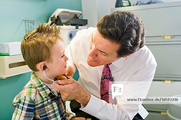Male doctor letting young boy play with stethoscope in doctor's office